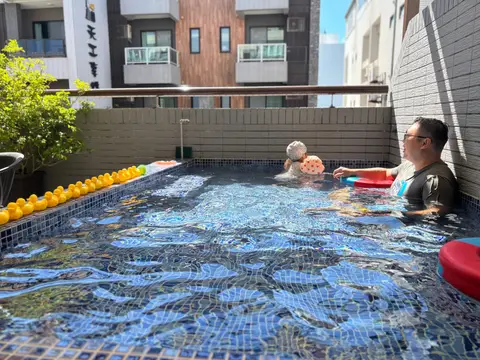 美夢成真陽台戲水池，大人在池裡陪小朋友玩水，池邊排著一整排黃色小鴨